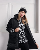 Frau in einem schwarz-weißen Pullover mit Leopardenmuster, einer schwarzen Steppjacke und einer zweifarbigen Mütze.