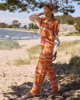 Frau in orange-weiß gemustertem Strickoberteil und passender Hose mit durchsichtigem weißen Schal.