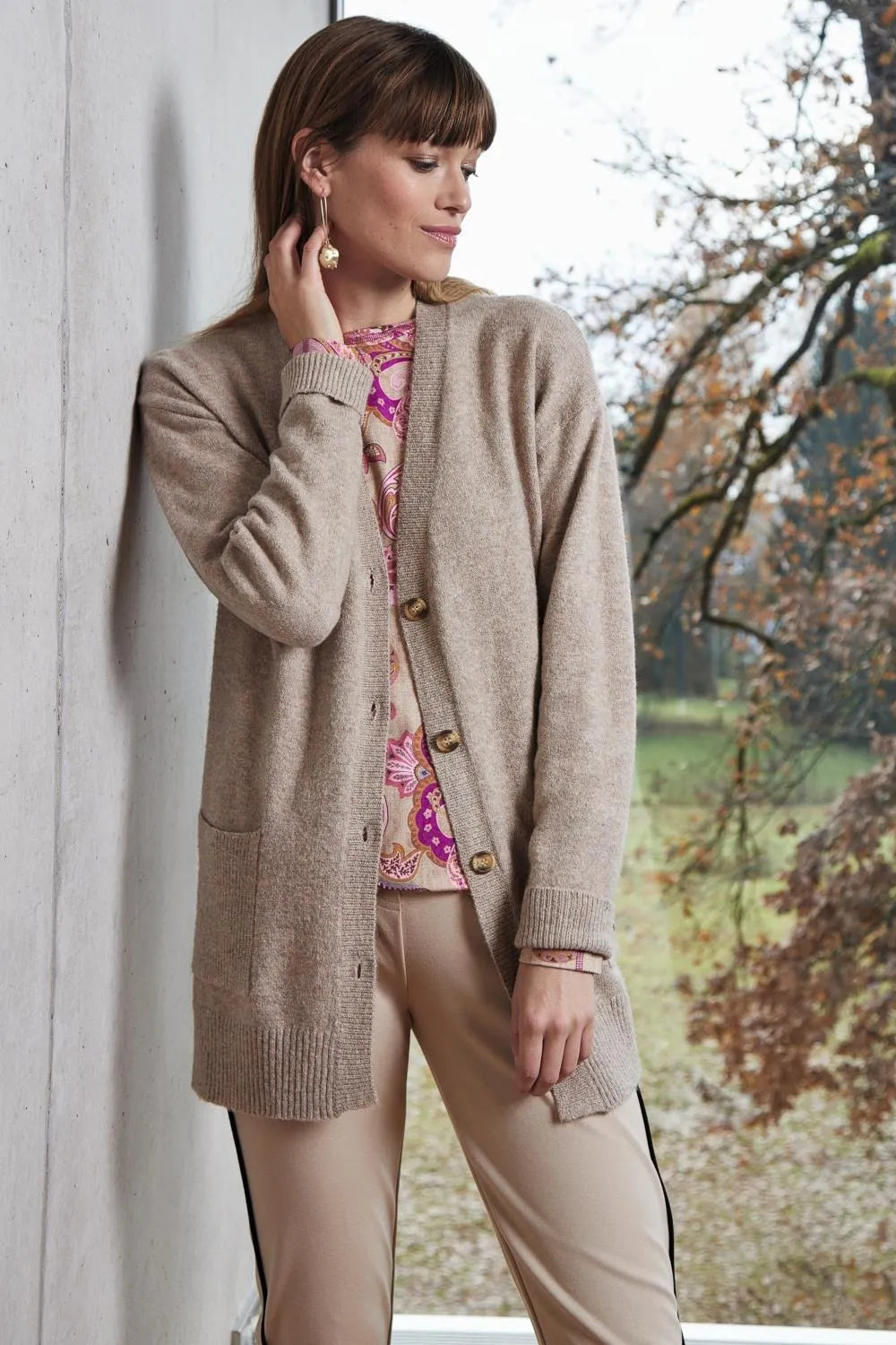 Beigefarbene langärmelige Strickjacke mit Taschen und Knöpfen, wahrscheinlich aus Wolle oder Baumwollmischung.