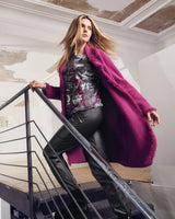 Eine Frau in einer magentafarbenen langen Strickjacke, einem dunkel gemusterten Oberteil und einer schwarzen Lederhose steigt eine Treppe hinauf.