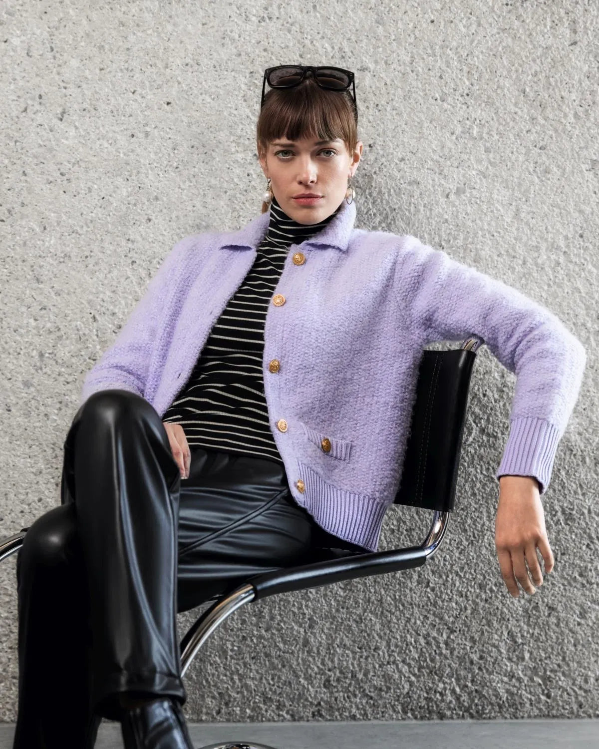 Lavendelfarbener, flauschiger Cardigan mit goldenen Knöpfen und schwarze Lederhose.