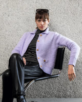 Lavendelfarbener, flauschiger Cardigan mit goldenen Knöpfen und schwarze Lederhose.