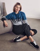 Frau trägt ein blaues, graues und schwarzes Sweatshirt mit Leopardenmuster und eine schwarze Hose mit Leopardenmuster.