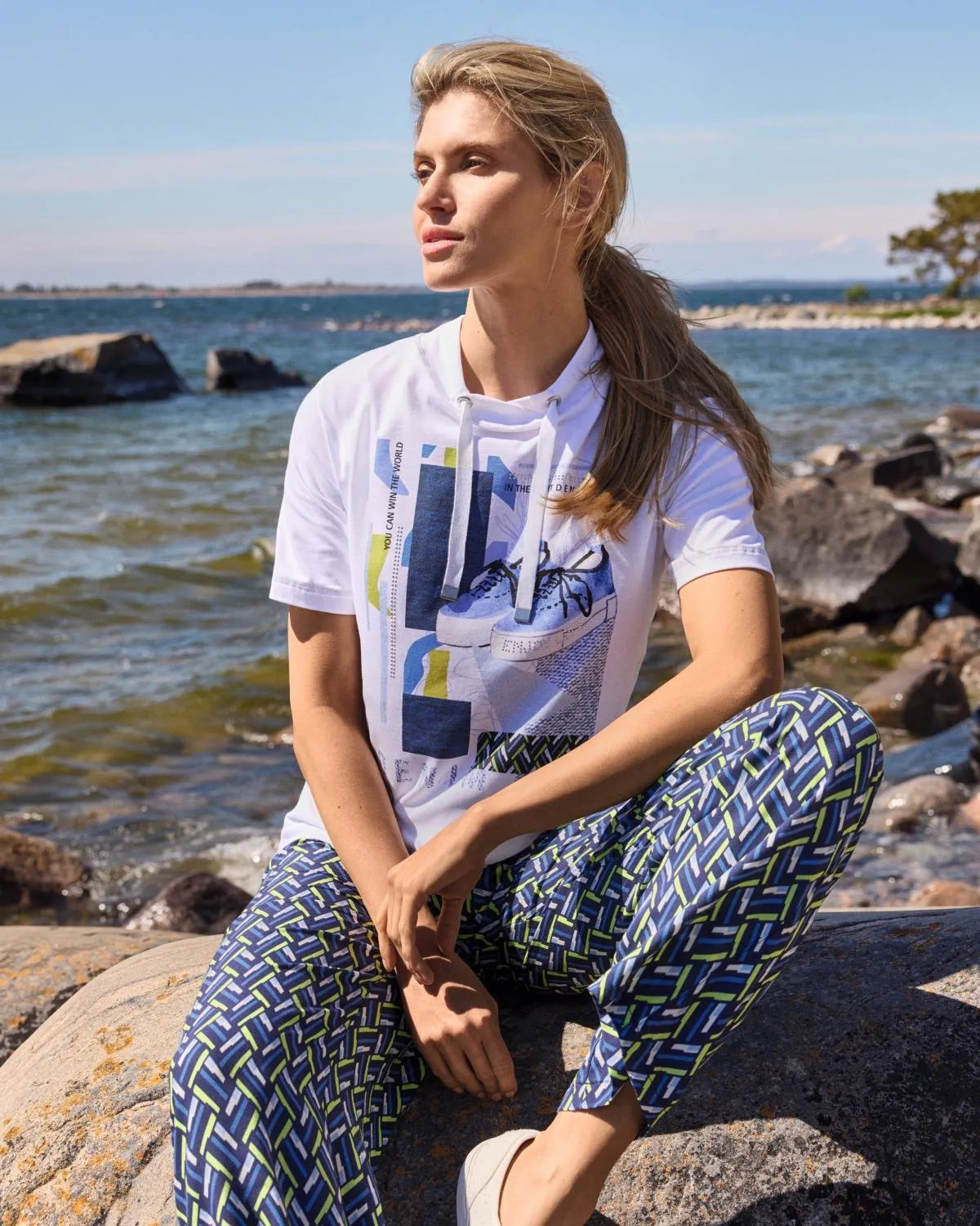 Weißes Grafik-T-Shirt mit blauer, geometrisch gemusterter Hose und Elfenohren.