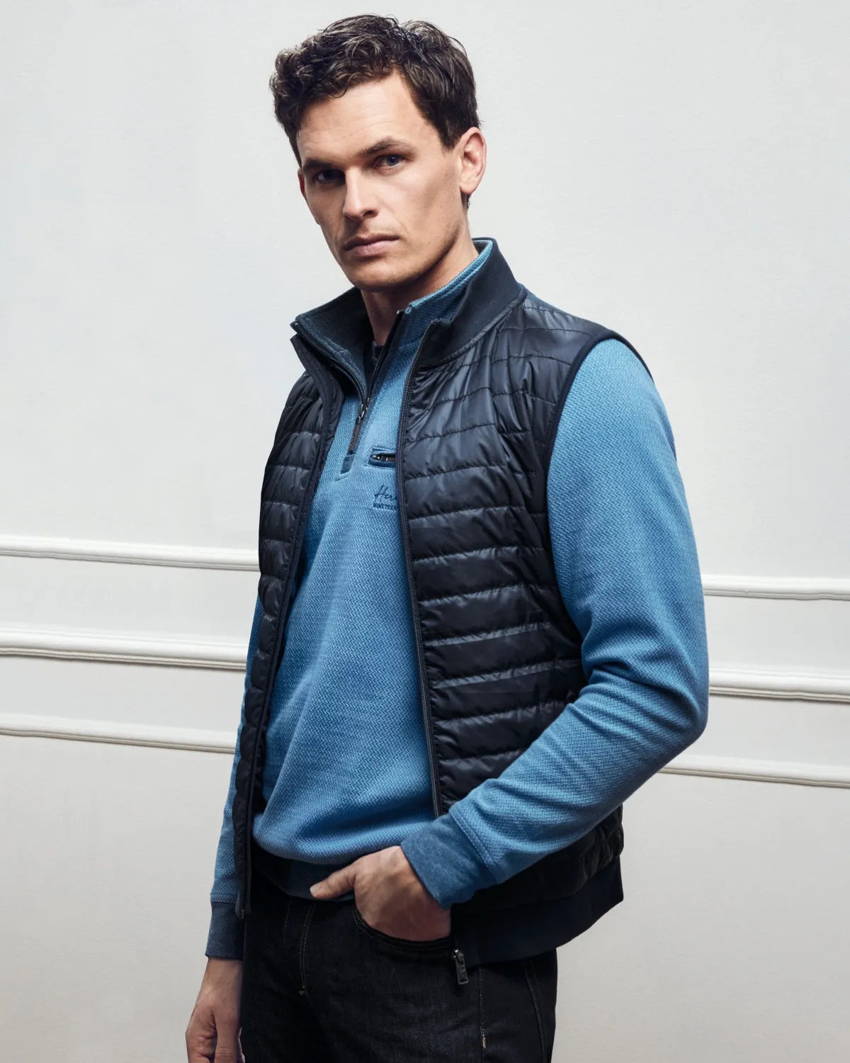 Dunkelblaue Steppweste für Herren über einem hellblauen, langärmeligen Poloshirt.