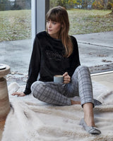 Schwarzes Sweatshirt mit der Aufschrift ’1984’’, karierte Pyjamahose und flauschige Hausschuhe.